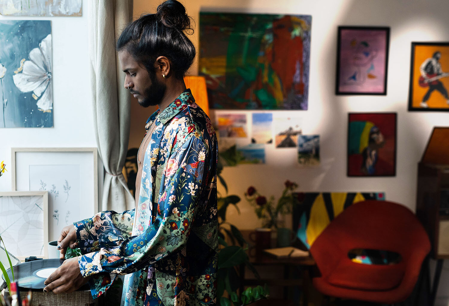 A man is playing a record player in his living space. His space has an eclectic aesthetic that is also warm and can easily be achieved through budget-Friendly creative home solutions.