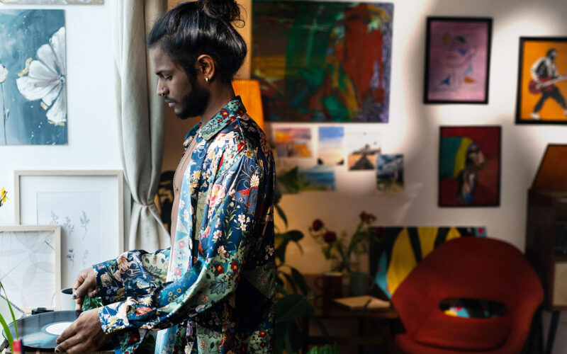 A man is playing a record player in his living space. His space has an eclectic aesthetic that is also warm and can easily be achieved through budget-Friendly creative home solutions.